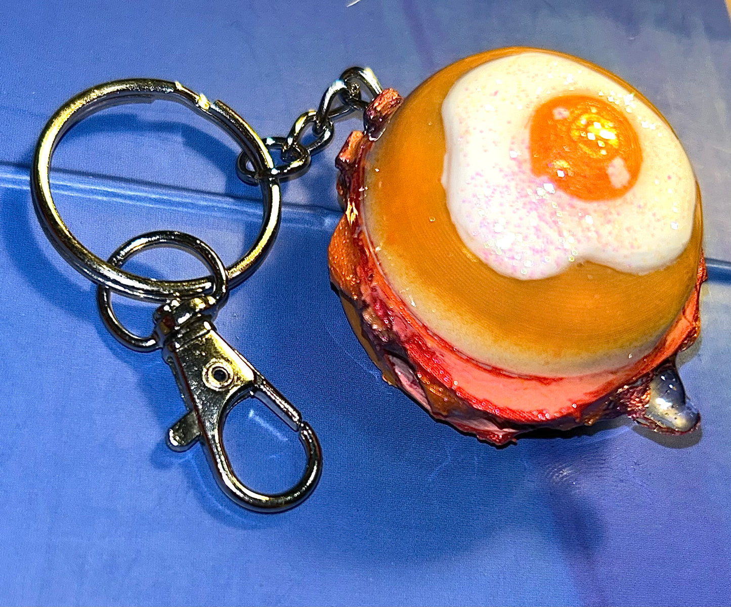 Keychain shaped like a breakfast burger with a bun, meat, and egg on a blue background