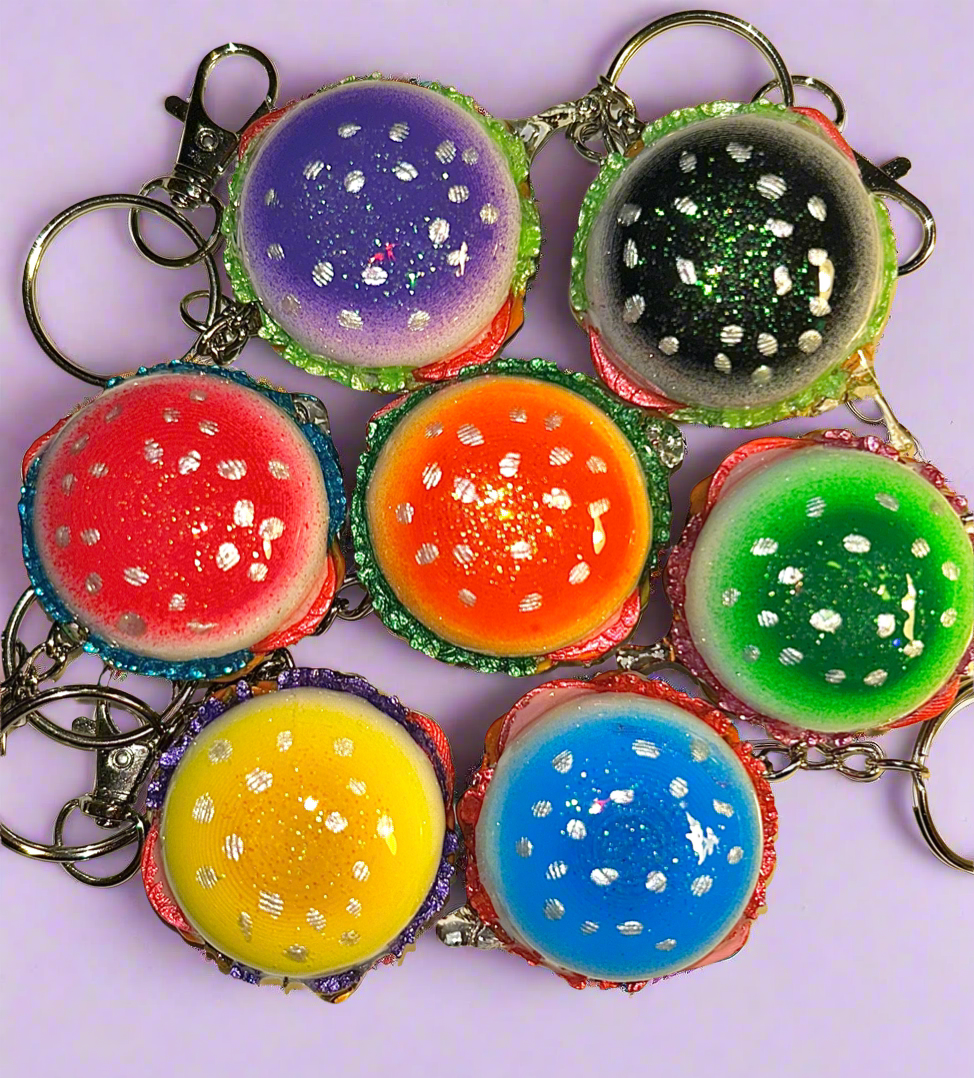 colorful burger keychains of orange, pink, yellow, green, blue, purple and black in a circle on a light lavender background