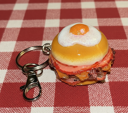 Keychain shaped like a breakfast burger with an egg on top on a red and white checkered tablecloth.
