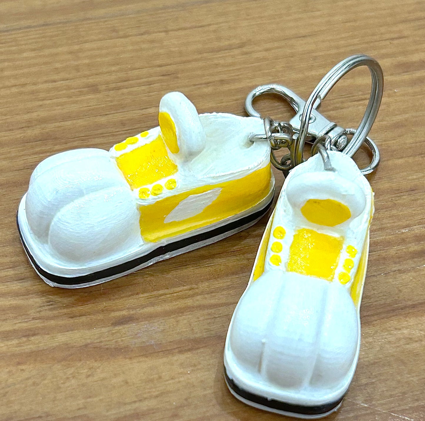 Keychain shaped like cartoon shoes with yellow and white design on a wooden background