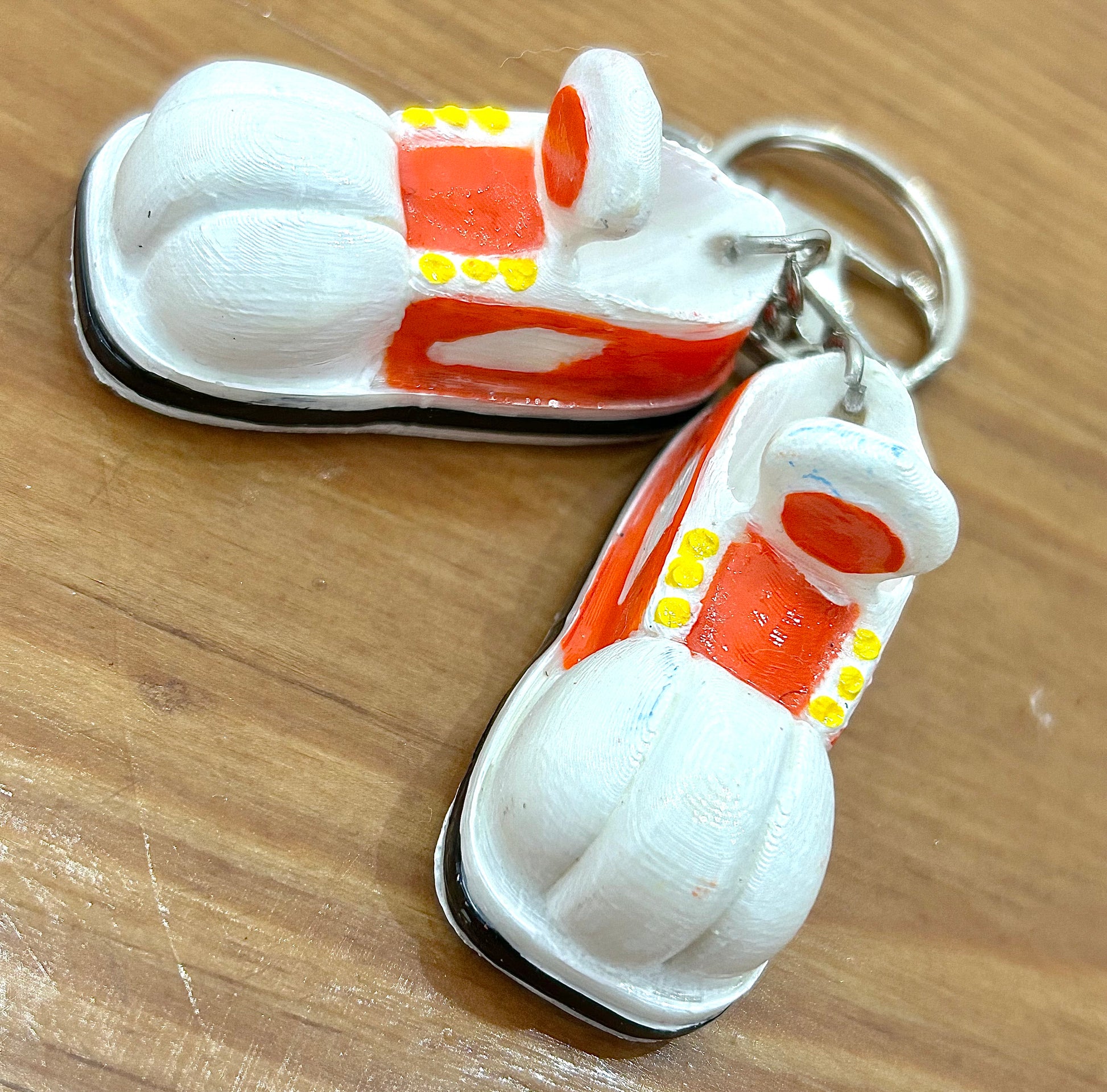 Keychain shaped like cartoon shoes with orange and white design on a light wooden background