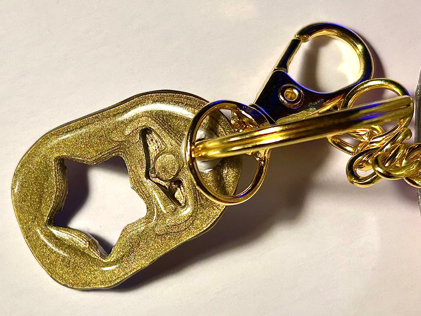 Gold soda tab attached to soda keychain on a white background