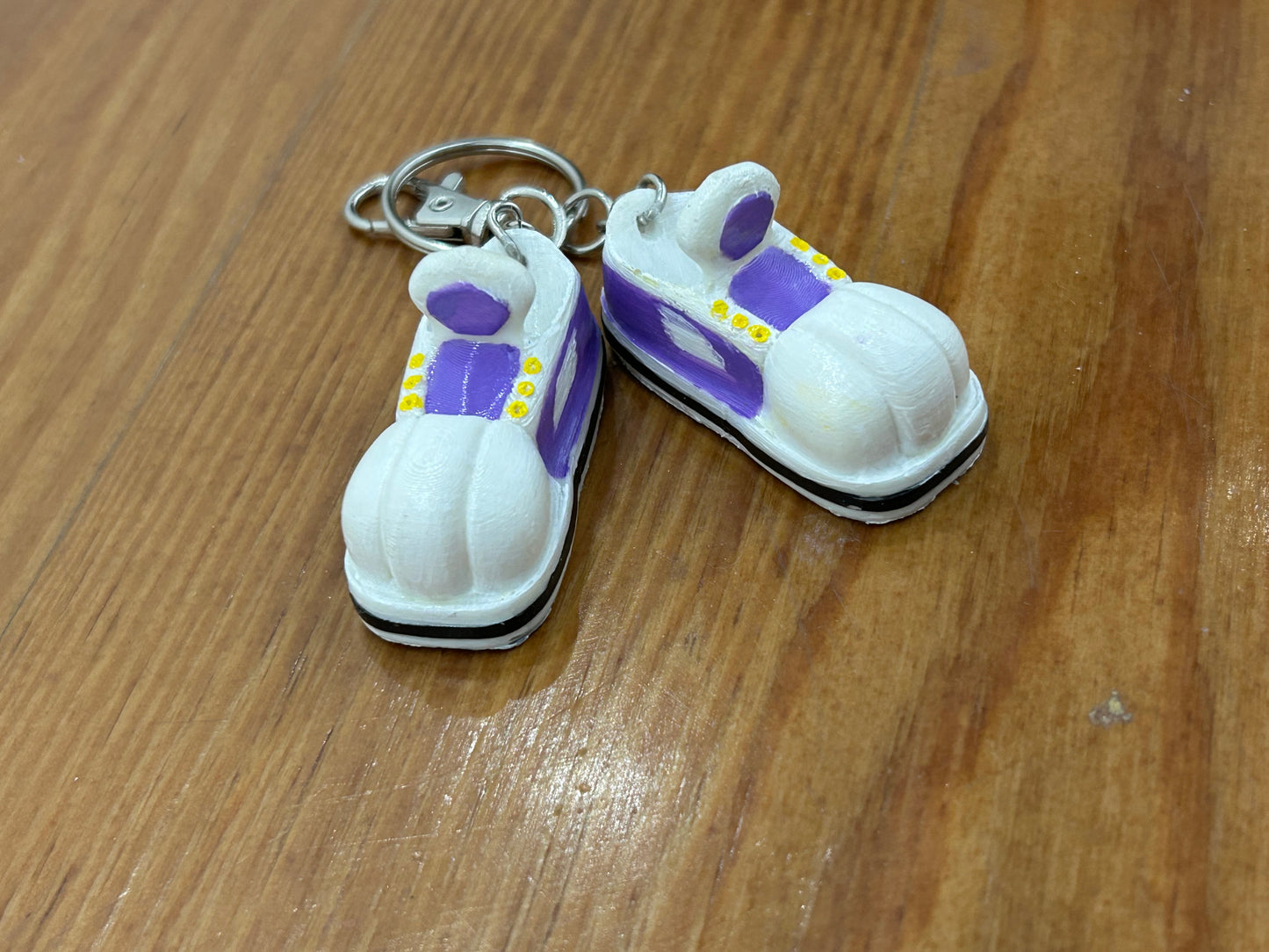 Keychain shaped like cartoon shoes with purple and white design on a light wooden background.