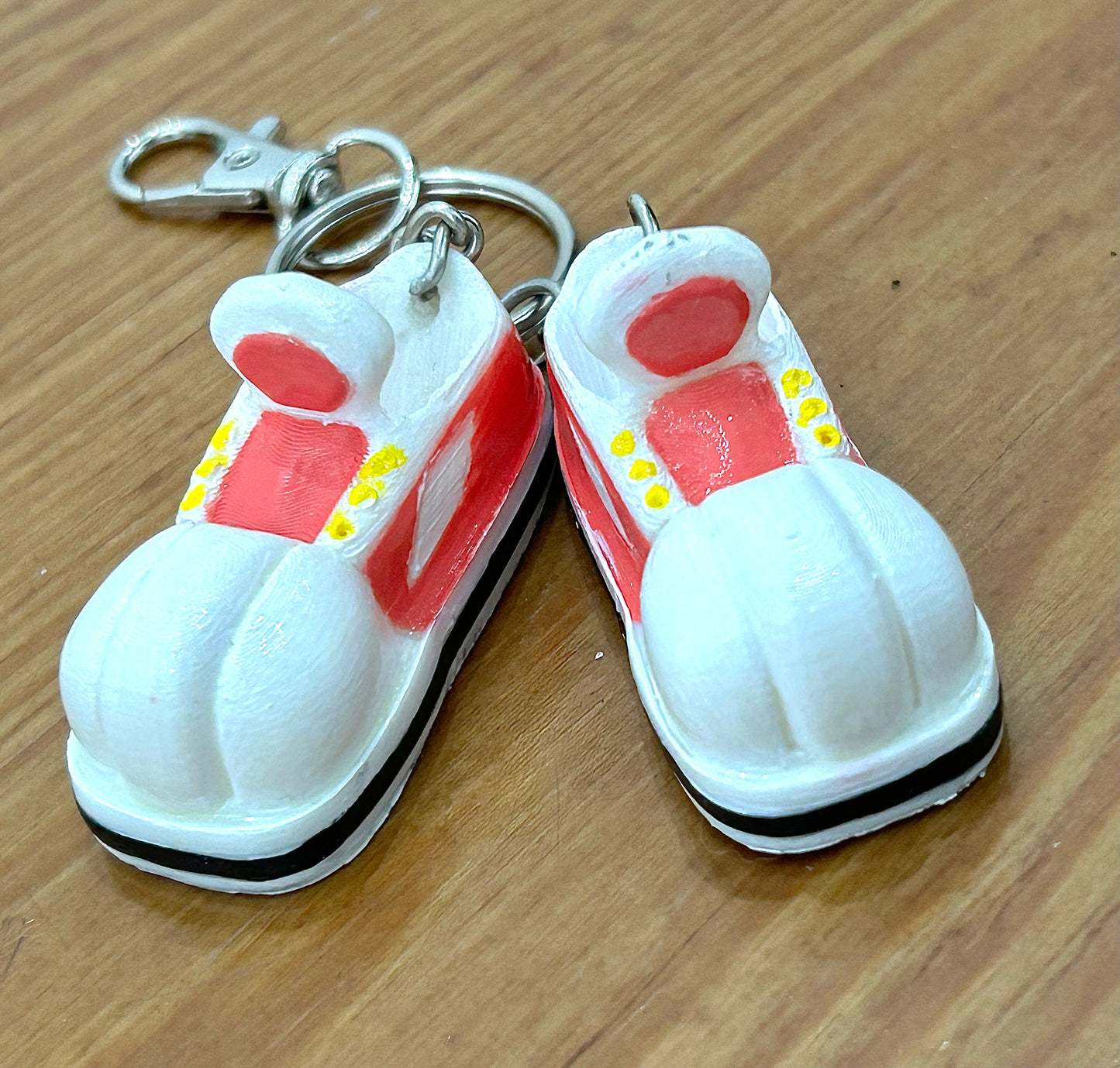 Keychain shaped like cartoon shoes with pink and white design on a light wooden background.