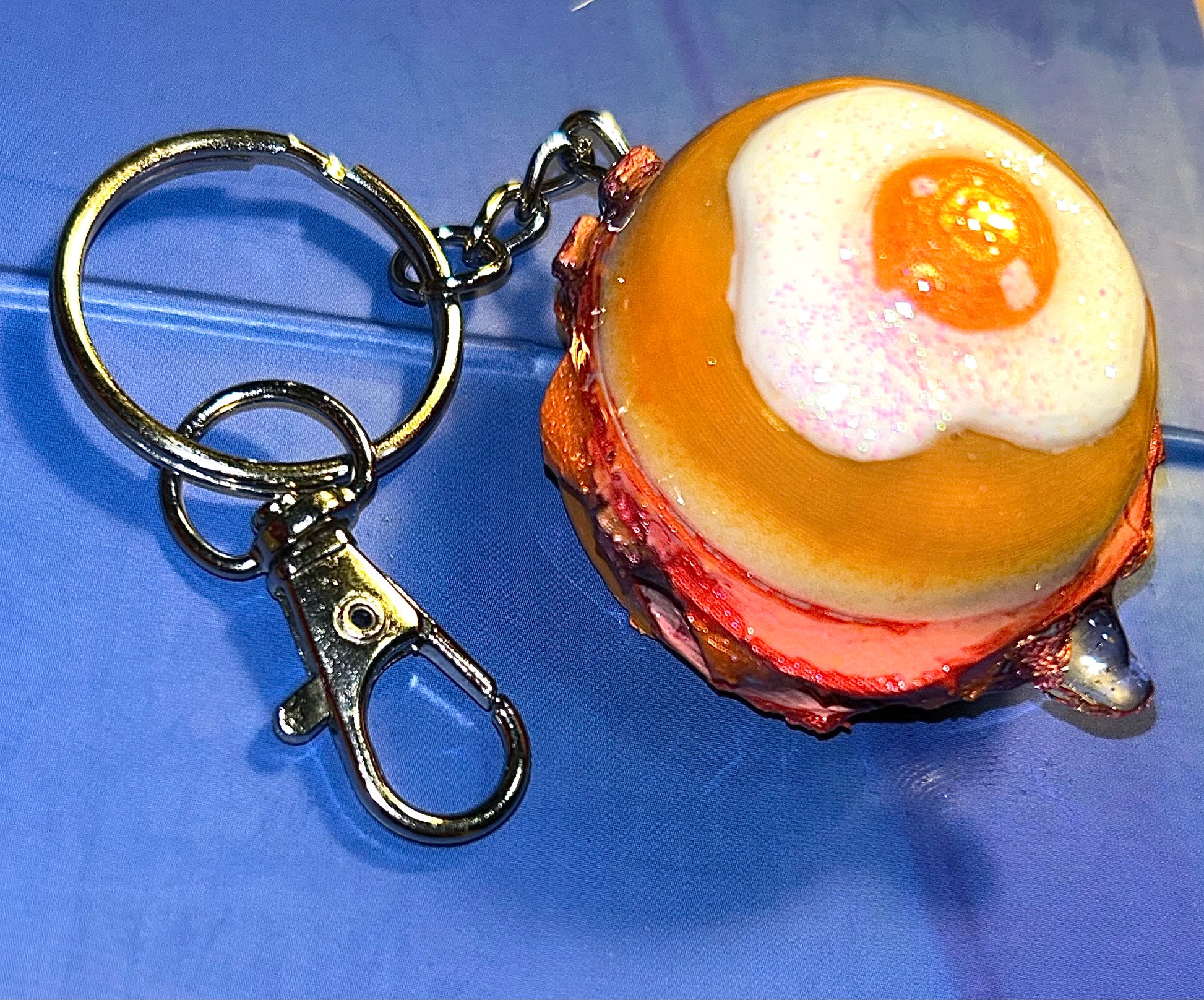 Keychain shaped like a breakfast burger with a bun, meat, and egg on a blue background